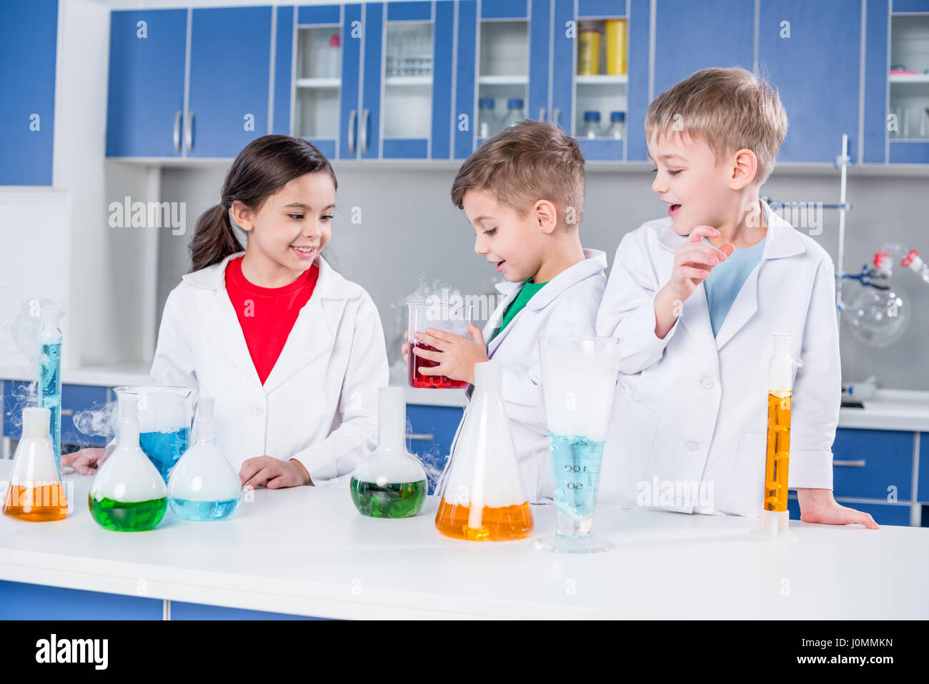 Drei Kinder in weißen Kitteln machen chemischen experimentieren im Labor Stockfoto