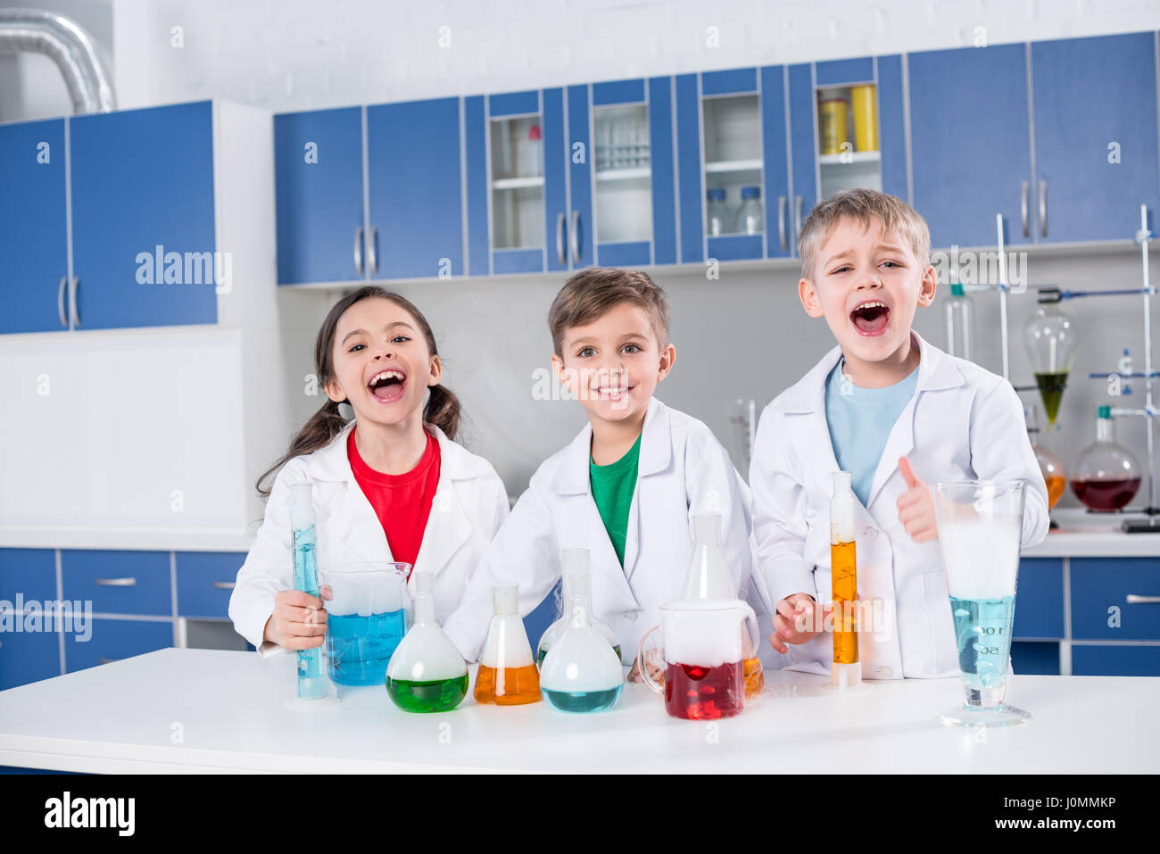 Drei glückliche Kinder in weißen Kitteln machen chemischen experimentieren im Labor Stockfoto