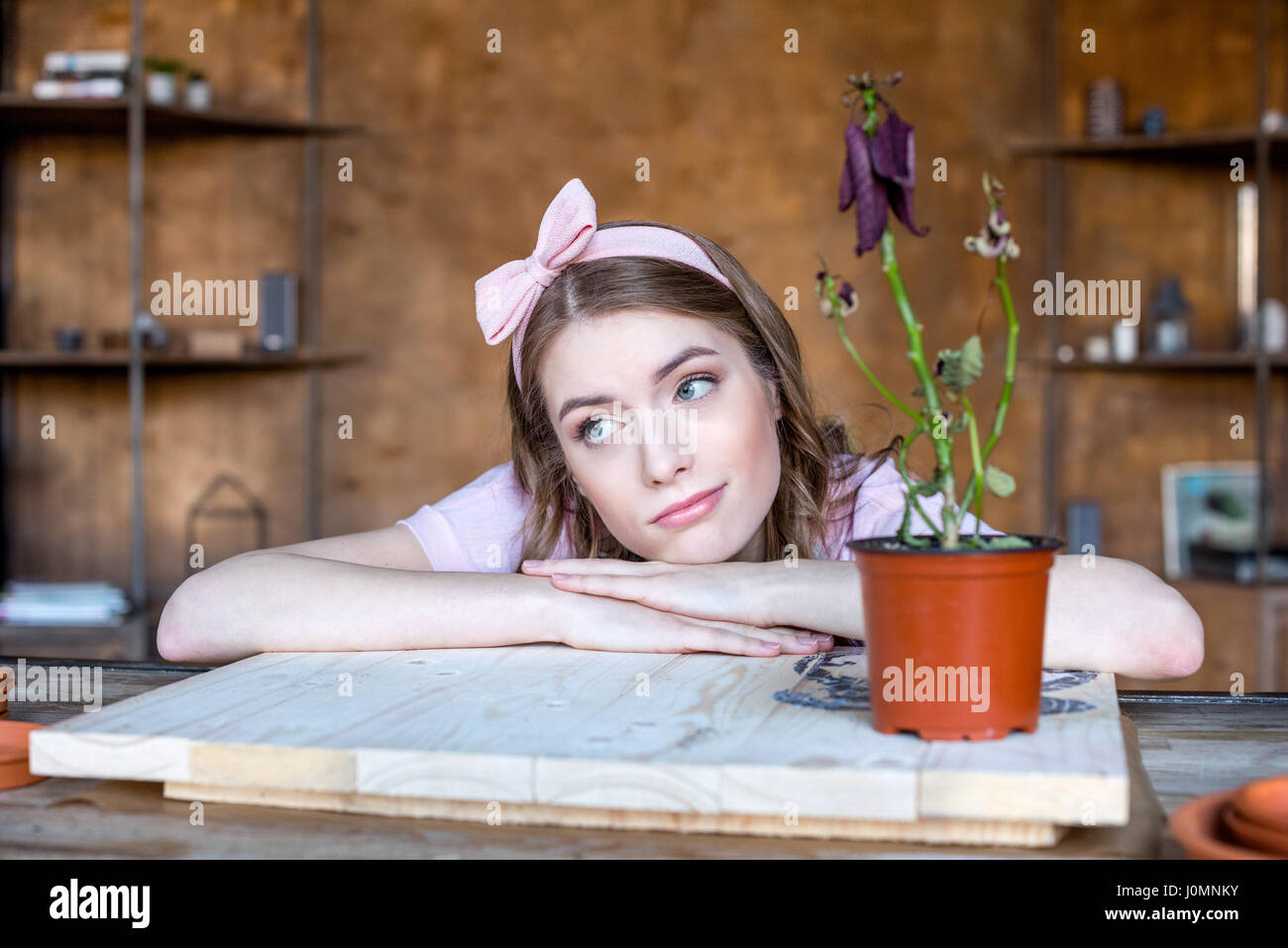 nachdenkliche junge Frau mit Pflanze im Blumentopf auf Tisch Stockfoto