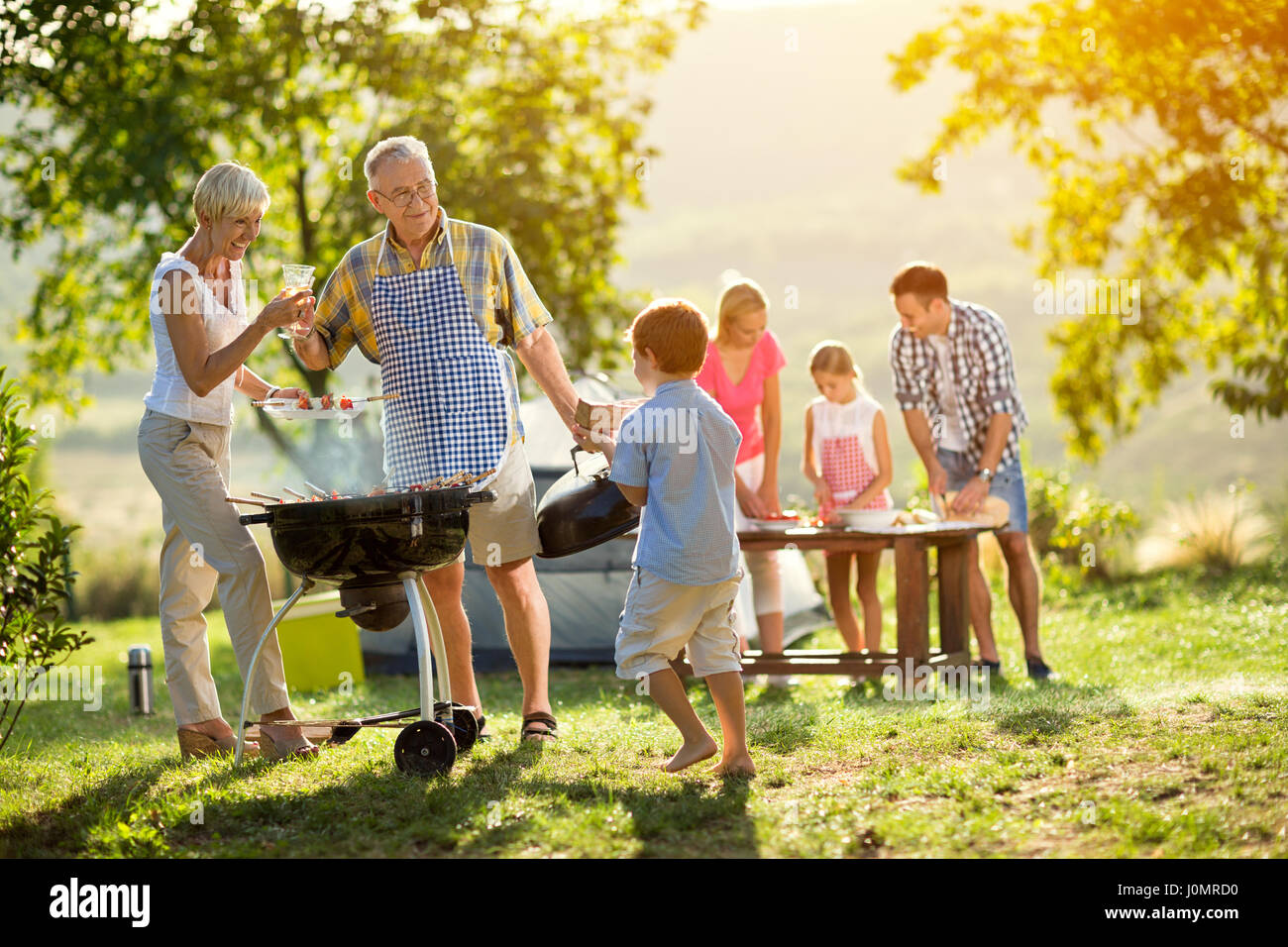 Enkel hilft Großeltern zu einem Grill für die Familie Stockfoto