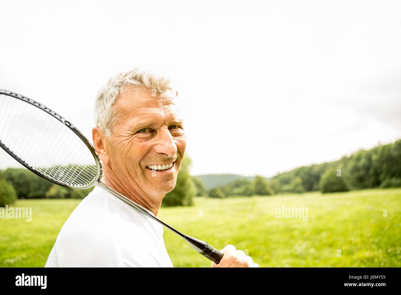 Älterer Mann, Badmintonschläger, lächelnd. Stockfoto