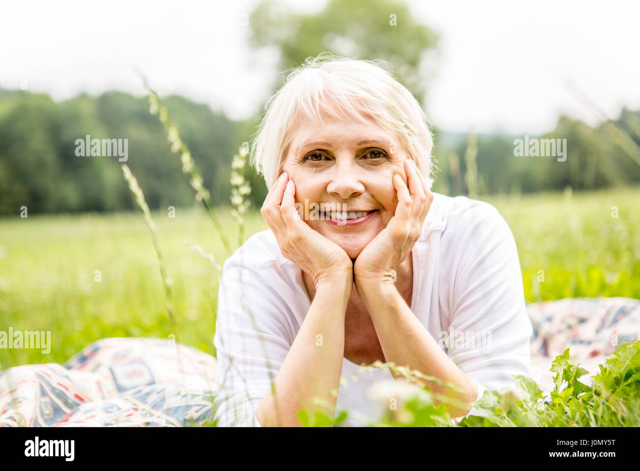 Senior liegende Frau auf Gras mit den Händen auf das Kinn. Stockfoto