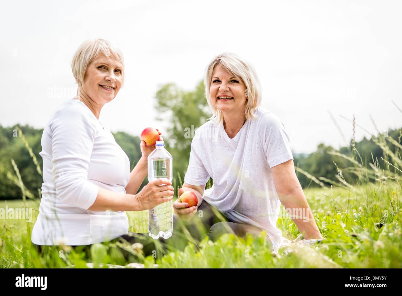 Zwei Frauen sitzen auf Gras mit Äpfel und Wasser. Stockfoto