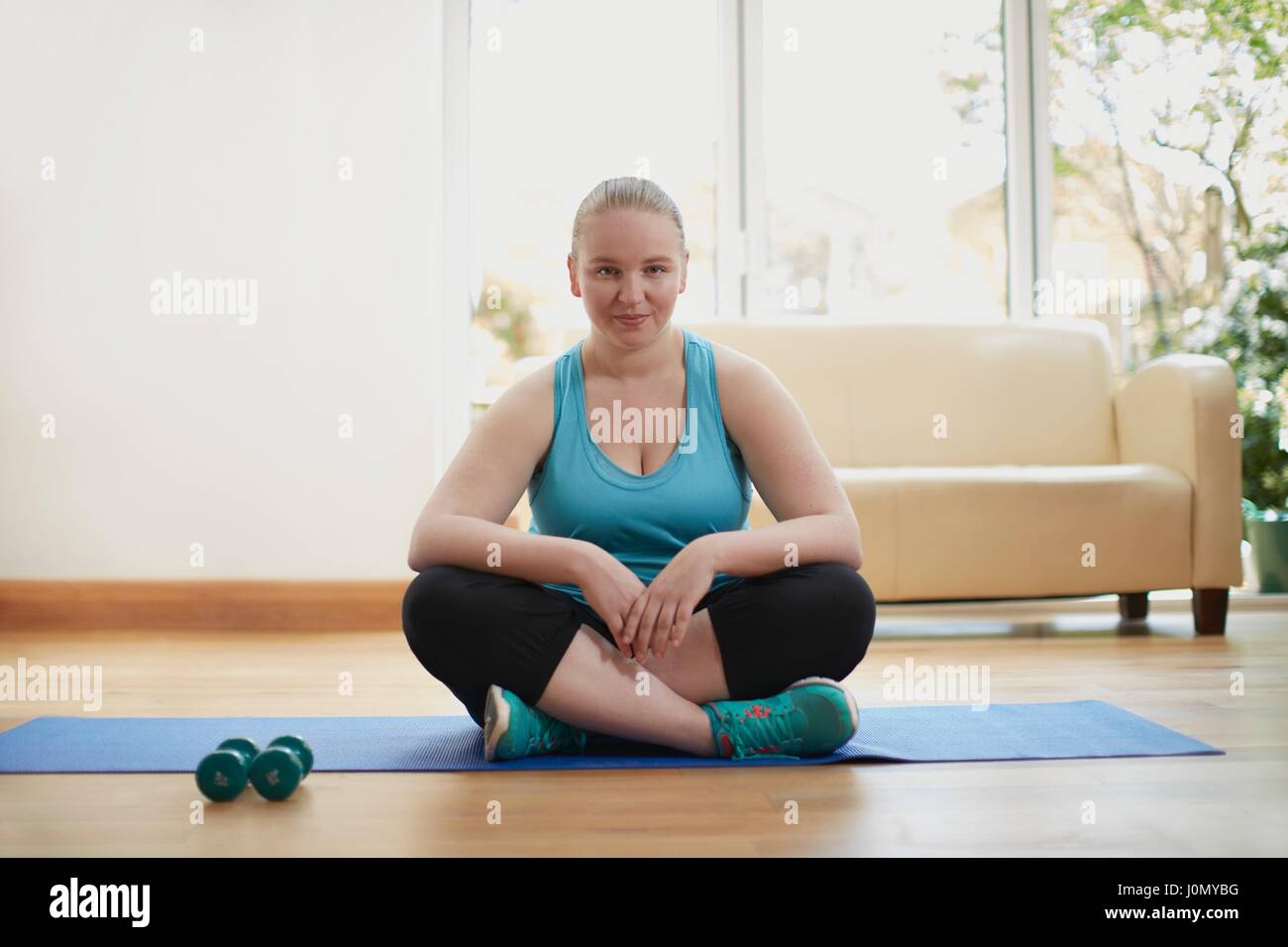 Junge Frau sitzt Schneidersitz auf Yoga-Matte. Stockfoto