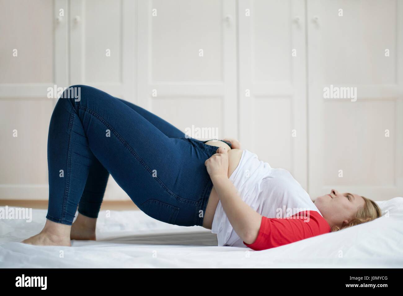 Junge Frau auf Bett versucht, Schaltfläche "Jeans. Stockfoto