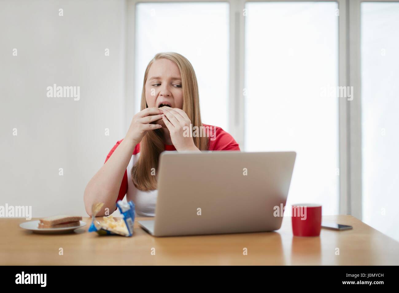 Junge Frau mit Laptop Sandwich zu essen. Stockfoto