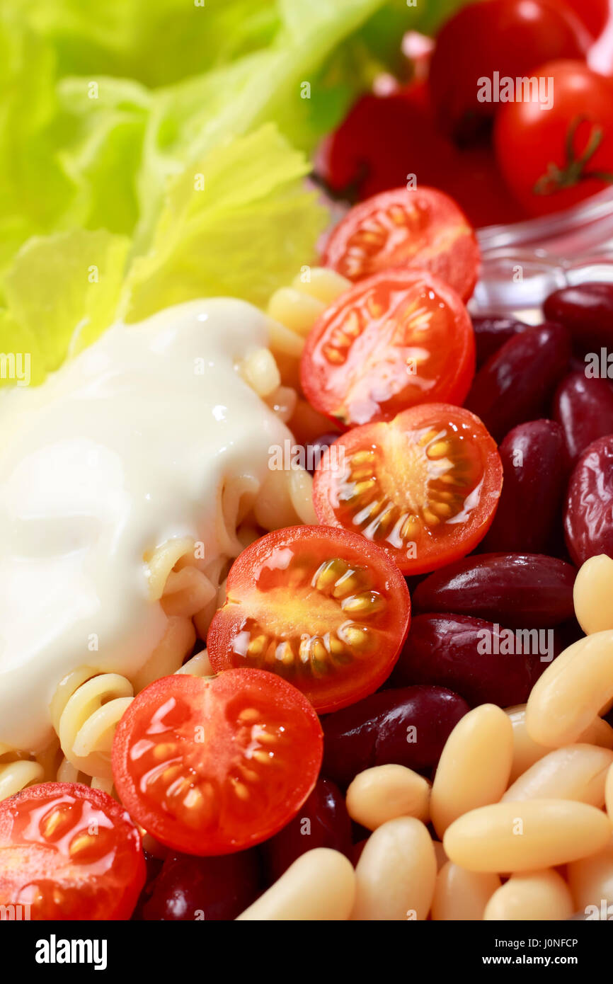 Gemüsesalat Nahaufnahme. Weiße und rote Bohnen, Cherry-Tomaten, Pasta, Salat und Creme. Stockfoto