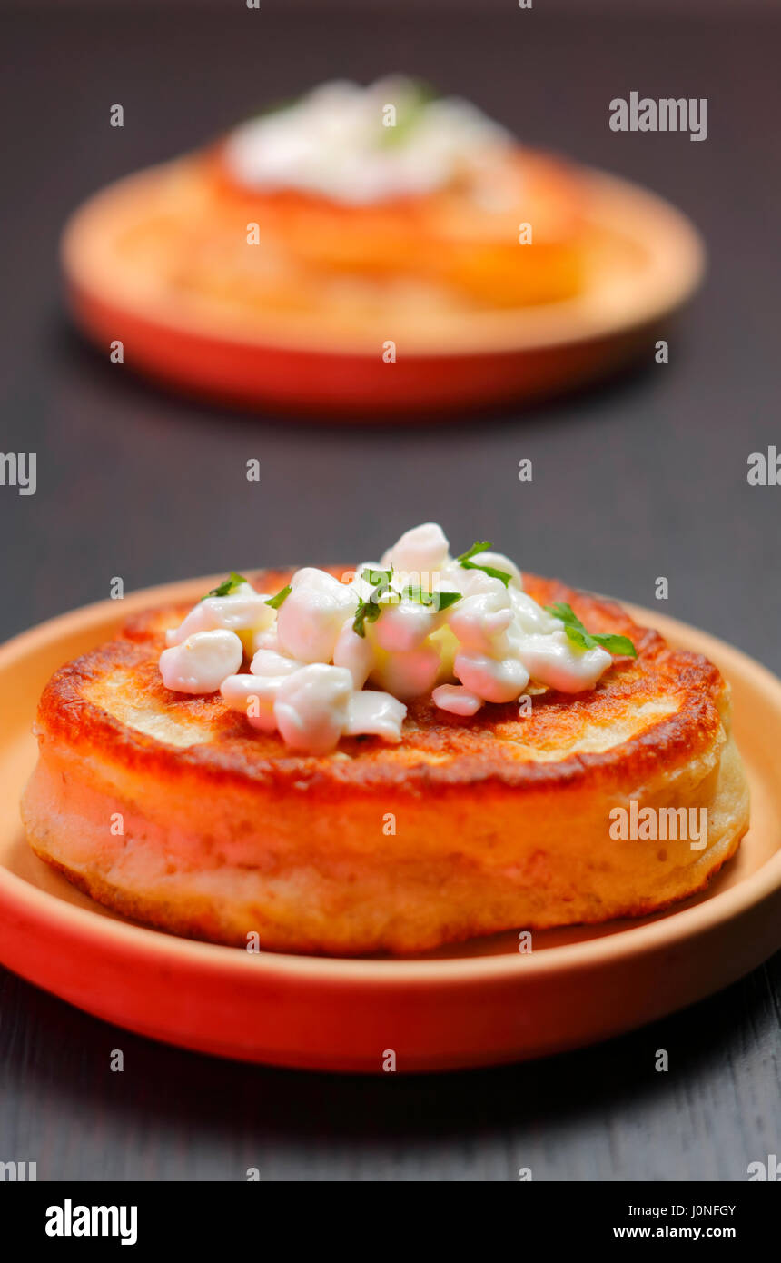 Blini (aus Weißmehl) mit Hüttenkäse und gehackte Petersilie Topping auf Ton Platte mit unscharfen Hintergrund Stockfoto