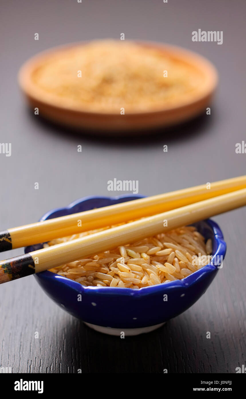 Brauner Reis in blau Schüssel mit Stäbchen auf unscharfen Hintergrund Stockfoto