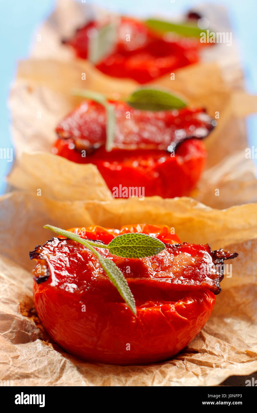 Gebratene Tomaten Hälften mit Speck und Salbei auf braune Blätter in einer Reihe Stockfoto