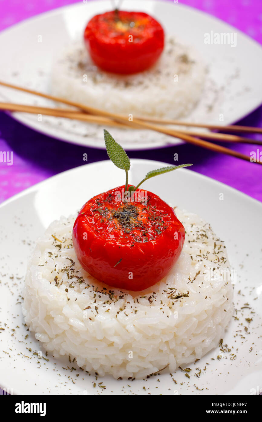 Fried halbierte Tomaten mit Salbei Zweig und pulverisierte Kräuter auf geformten Reis. Geringe Schärfentiefe. Stockfoto