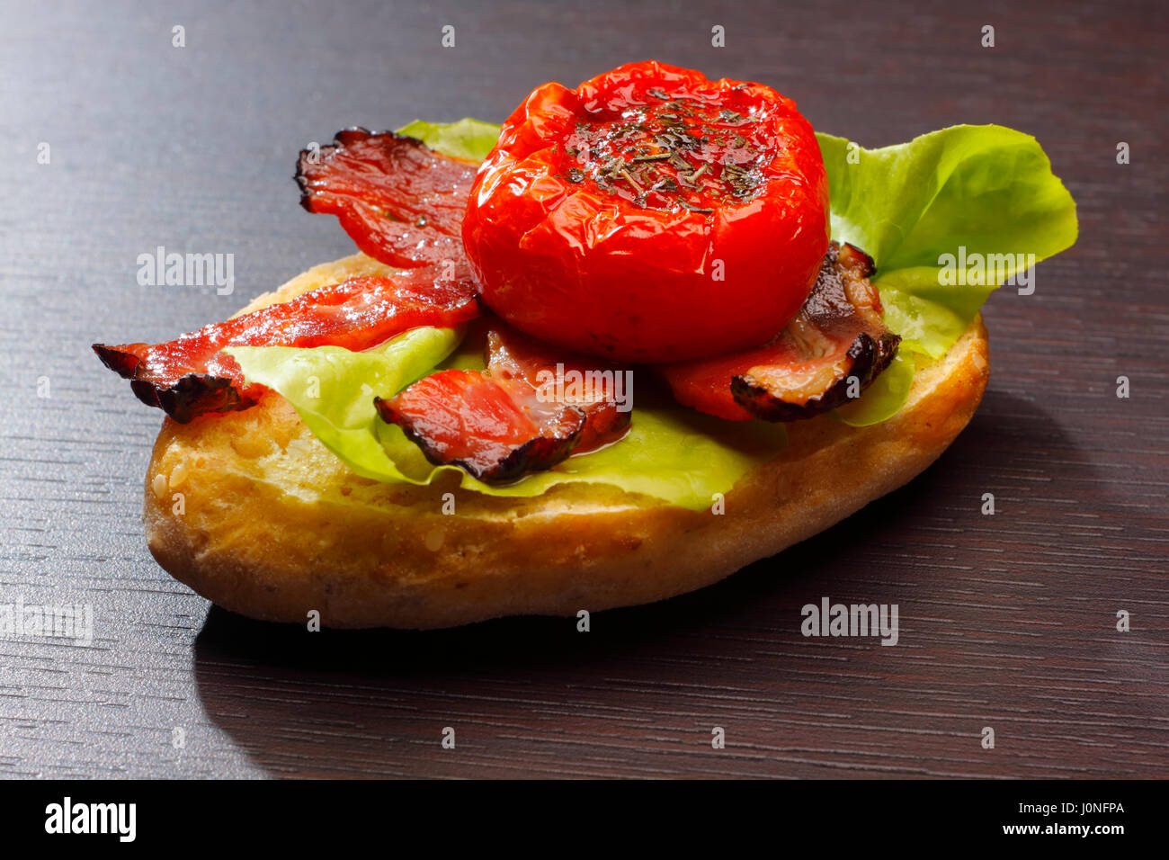 Ein halbes Brötchen mit gebratenem Speck, halbierte Tomaten und Salat Stockfoto