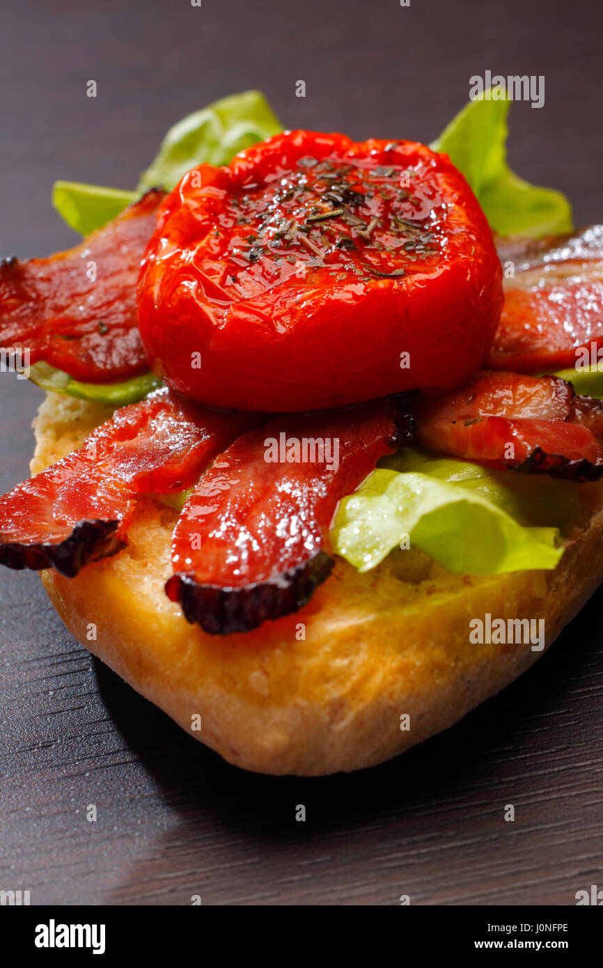 Ein halbes Brötchen mit gebratenem Speck, halbierte Tomaten und Salat Stockfoto