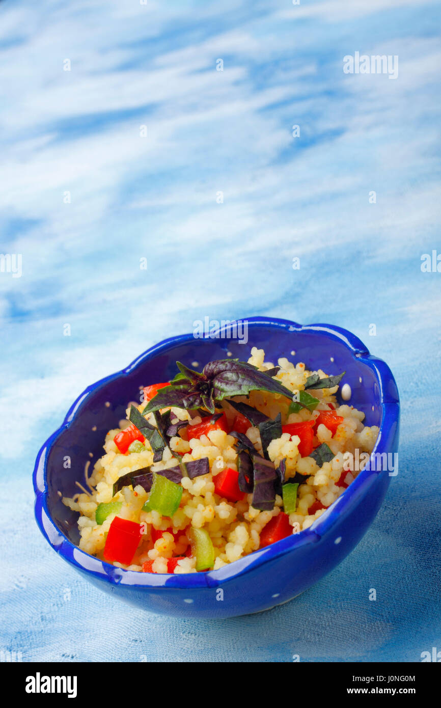 Schale mit Couscous, gehackten Paprika und roter Basilikum auf blau bemalte Textilien Hintergrund Stockfoto