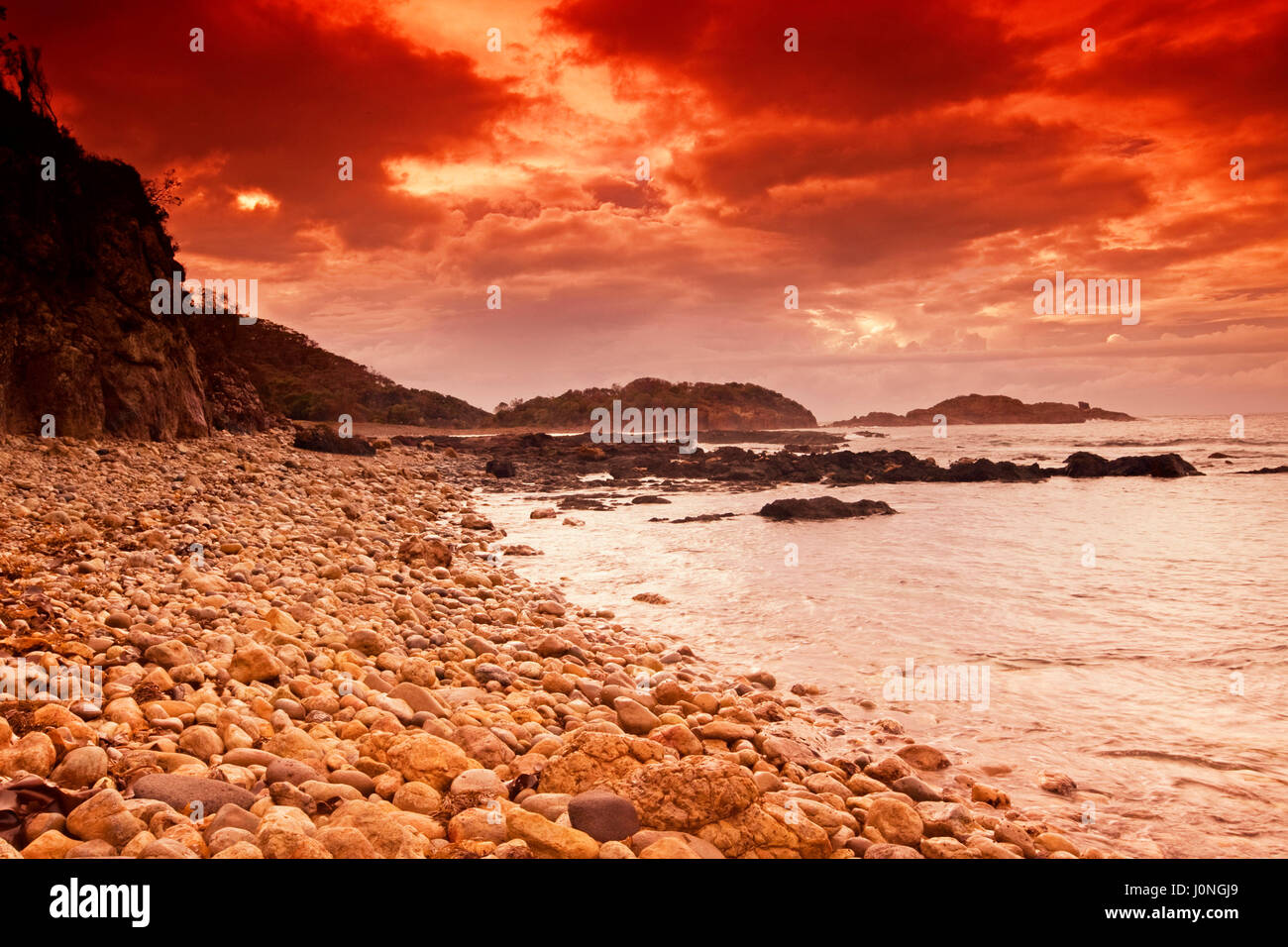 Steiniger Strand, Klippen und Pazifischen Ozean unter roter Himmel Sonnenuntergang im Mimosa Rocks National Park, NSW Australia Stockfoto