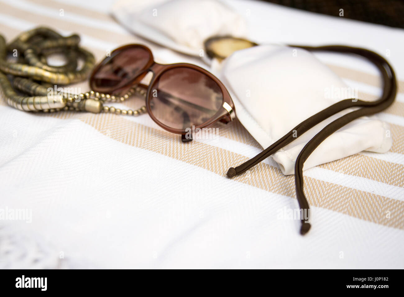 Das Konzept der Sommer Zubehör Nahaufnahme von weiß und Beige Farbe türkischen Pestemal, Weißgold Kette, Sonnenbrille und weißen Bikini-Oberteil mit braun Stockfoto