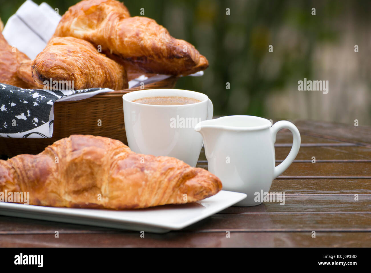 Croissants, Kaffee und Milch, auf einem Holztisch im Tageslicht. Stockfoto