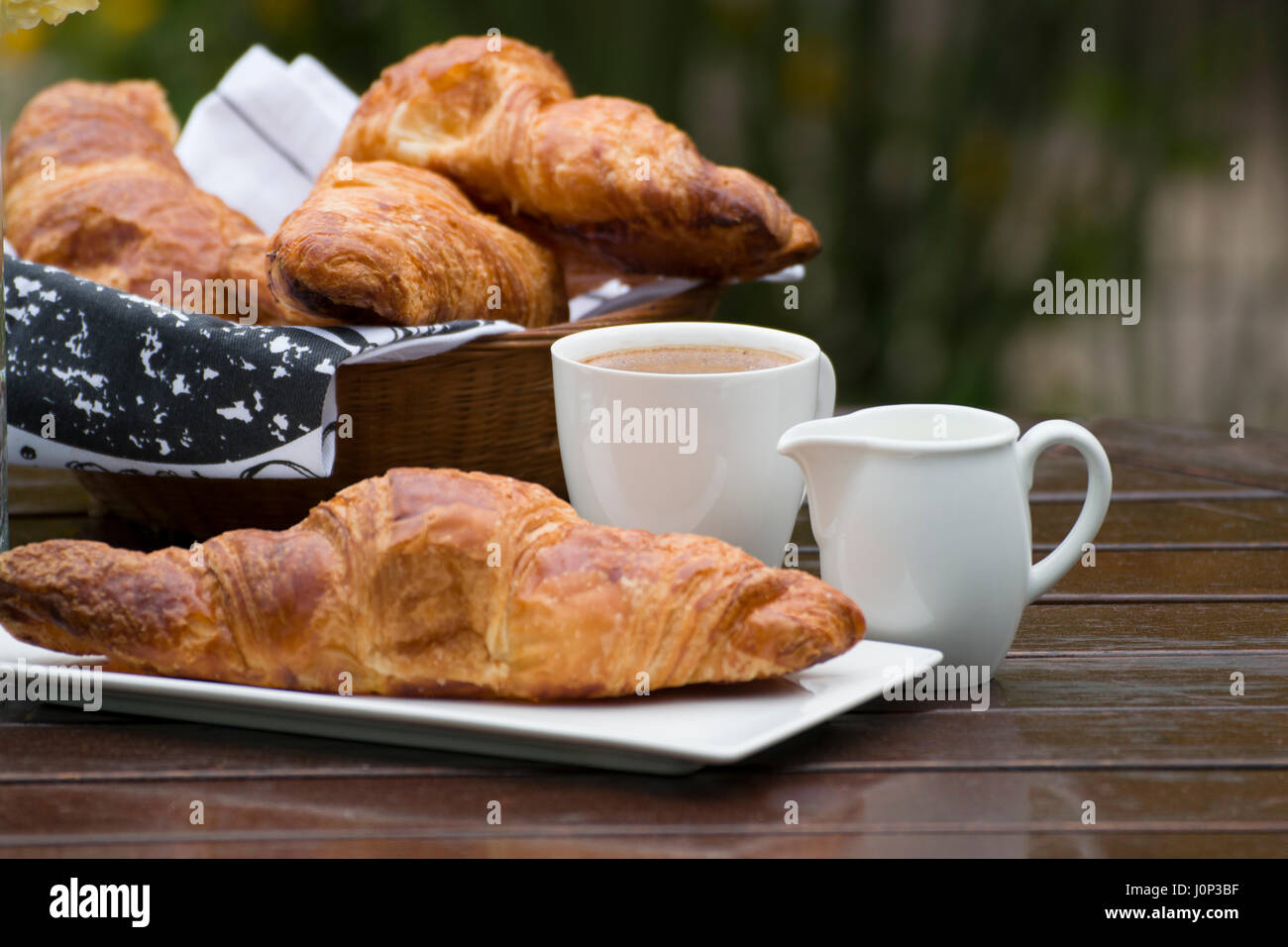 Croissants, Kaffee und Milch, auf einem Holztisch im Tageslicht. Stockfoto