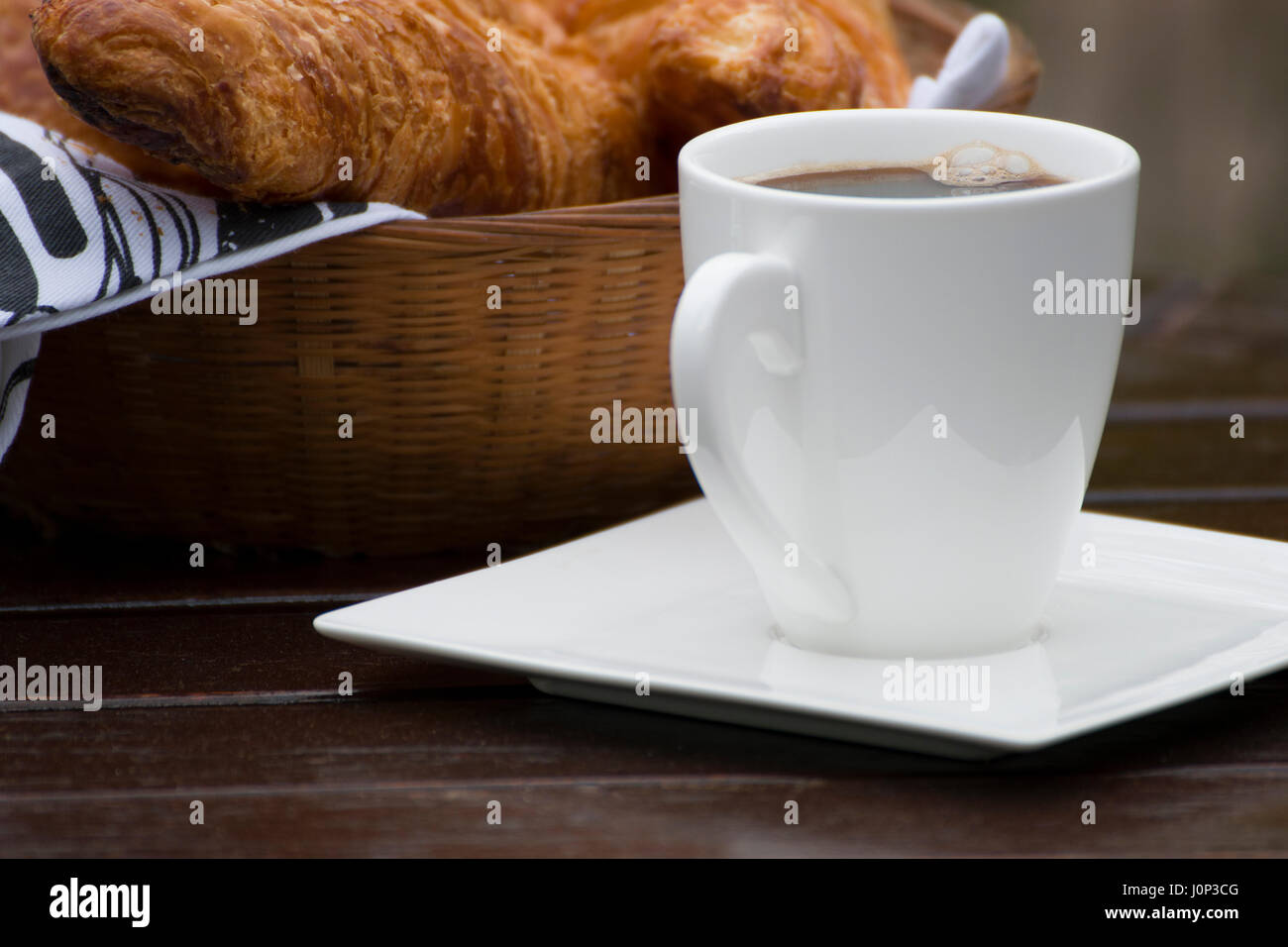 Eine Tasse Kaffee in der Nähe einen Korb mit französischen croissants Stockfoto