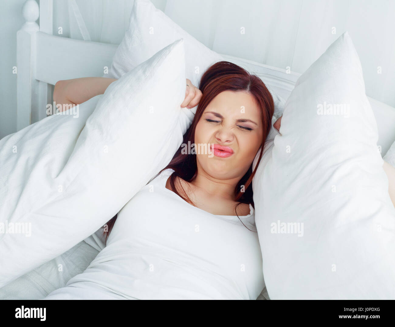 schöne junge Brünette Frau unglücklich über Lärm oder Schlaflosigkeit mit einem Kissen im Bett Stockfoto
