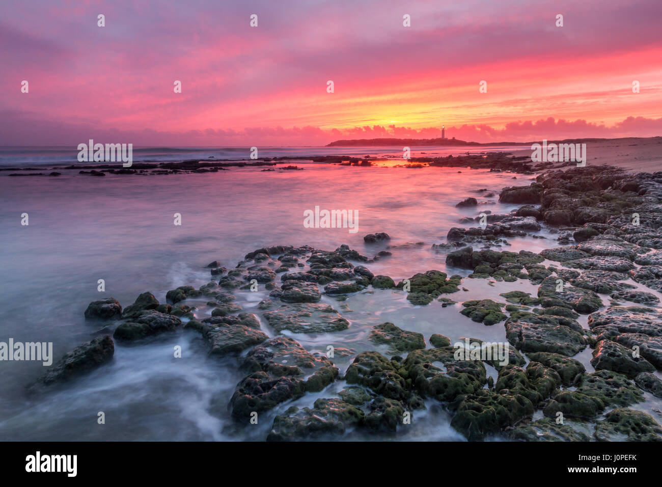 Letzten Lichter am Kap Trafalgar mit Wellen, die auf den Felsen und den Leuchtturm von Trafalgar im Hintergrund, Cadiz, Spanien Stockfoto