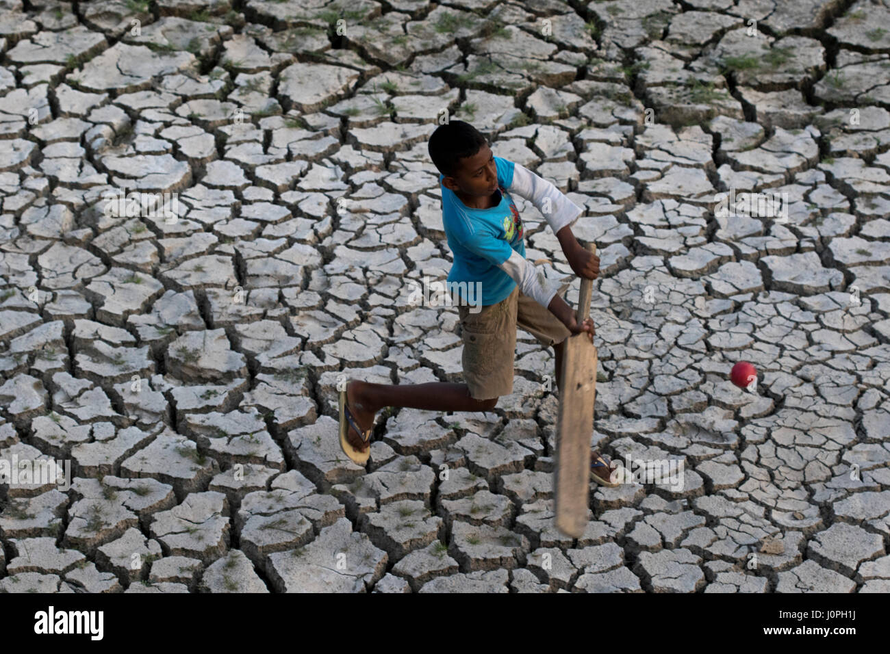 Ein Junge spielt Cricket auf einem Feld bei Beraid unter Dhakas Bhatara, die aufgrund der Trockenheit geknackt hat. Stockfoto
