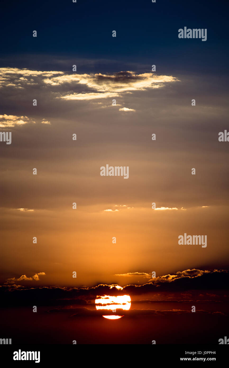 Silhouetted Wolken über eine perfekte runde Sonne schneiden Stockfoto