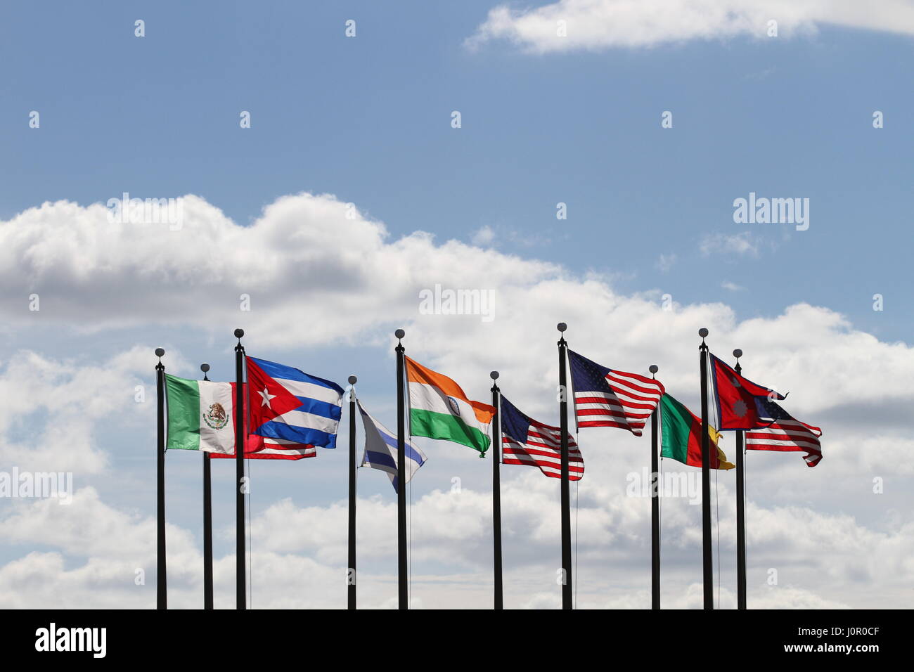 Die Flaggen USA, Nepal, Kamerun, Israel, Indien, Mexiko und Kuba auf einen Fahnenmasten im Wind gegen einen blauen Himmel und weiße Wolken. Der Wind weht. Stockfoto