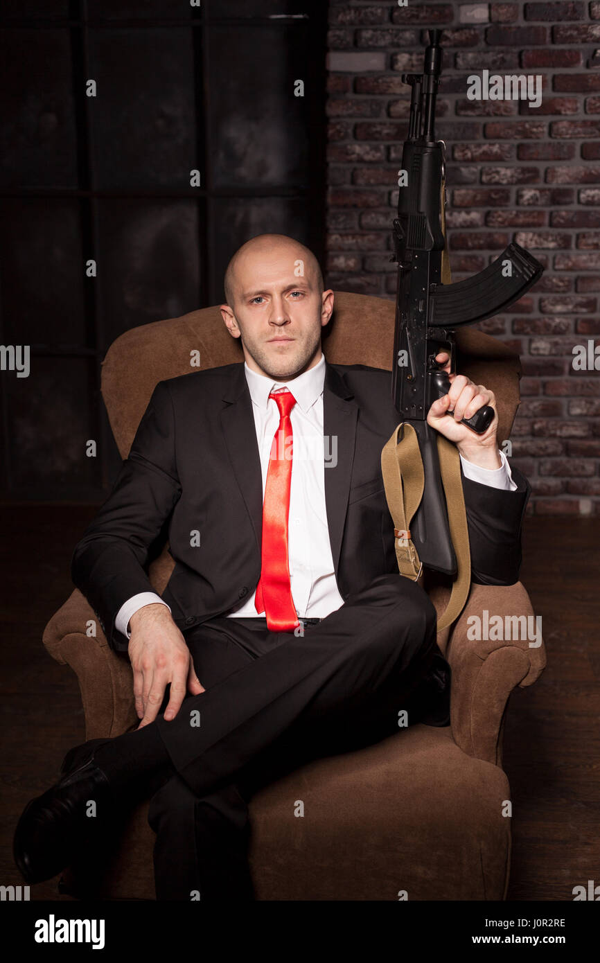 Auftragskiller in Anzug und roter Krawatte sitzt in einem Stuhl und hält  automatische Waffe. Mutige professionelle Geheimagenten auf mission  Stockfotografie - Alamy