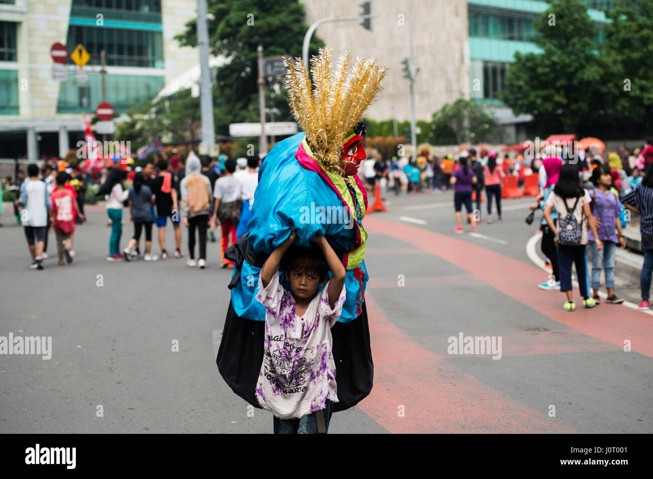 Jakarta. 16. April 2017. Ein Kind street Performer trägt seine Ondel-Ondel (Jakartas native Puppenkleid) auf der Straße nach Leistung während der autofreie Tag in Jakarta, 16. April 2017. Bildnachweis: Veri Sanovri/Xinhua/Alamy Live-Nachrichten Stockfoto