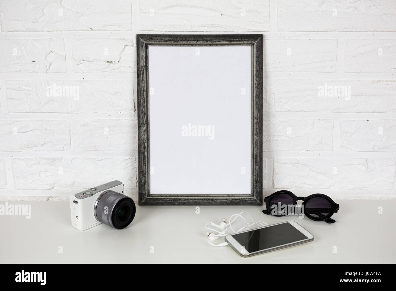 Weiße Mock Up und modernen Accessoires umrahmen. auf Ziegel Wand Hintergrund. Spiegellose Kamera, Handy mit Kopfhörer und Brille. Trendige Templa Stockfoto