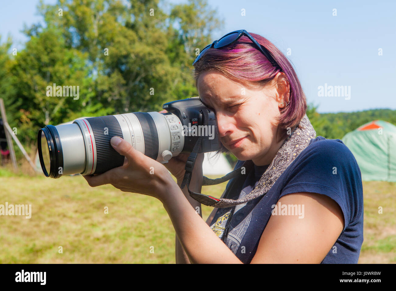 Eine junge Frau mit lila gefärbte Haare nimmt ein Foto mit einem Teleobjektiv. Stockfoto