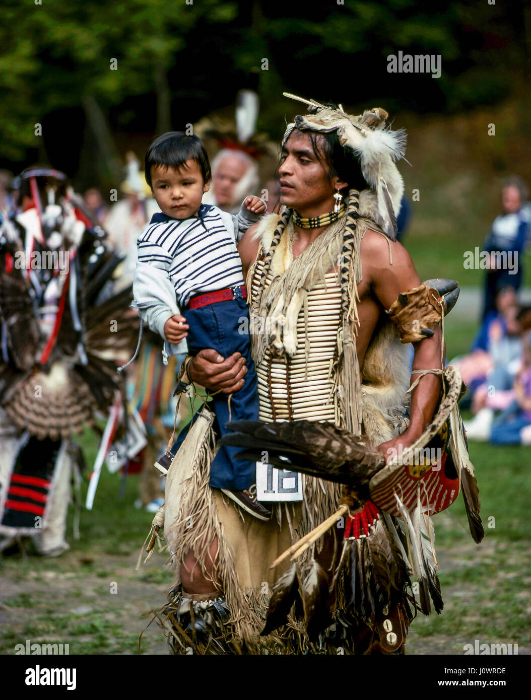 Eine Native American Indian Vater in tribal Kostüm tanzen auf einem Powwow seinen jungen Sohn Holding gekleidet. Hanover, NH, USA. Stockfoto