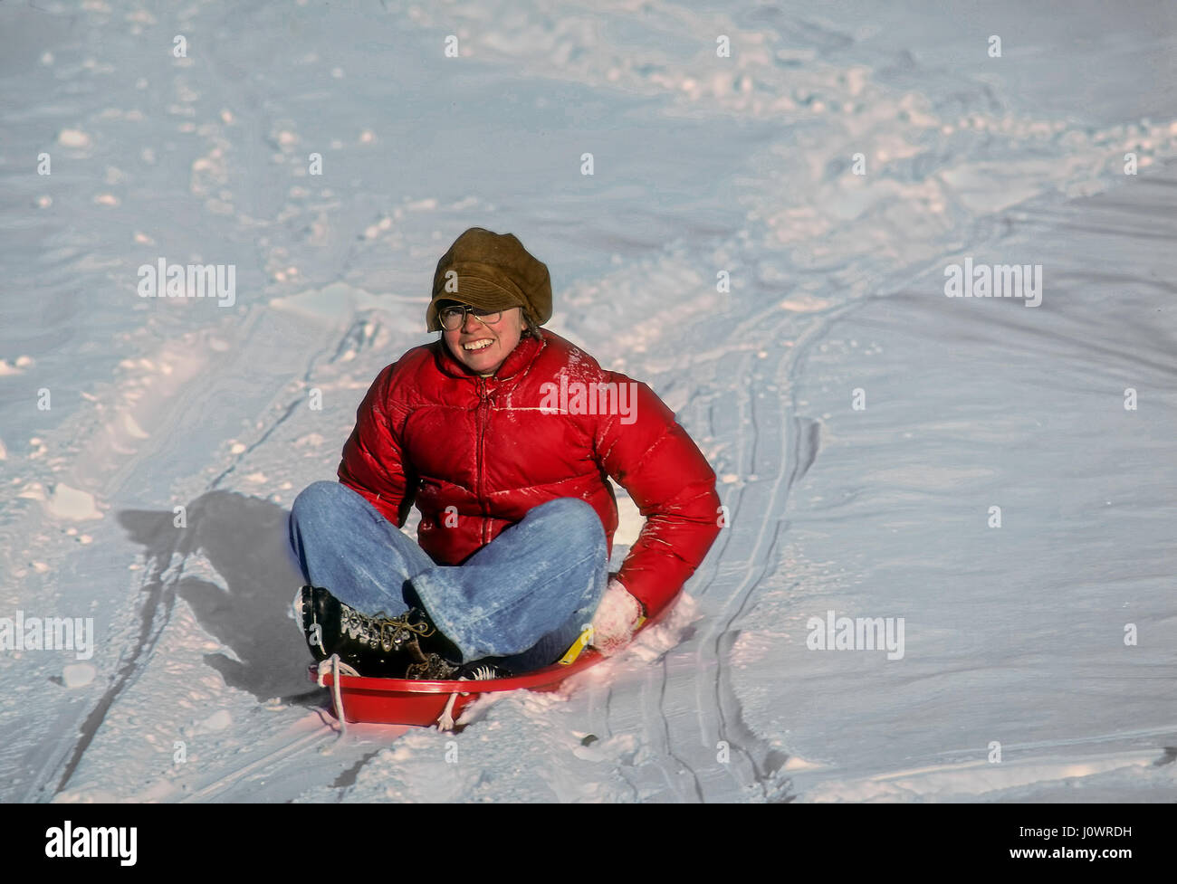 Erwachsene Frau in einem leuchtend roten Jacke rutscht hinunter einen Hügel auf einem Kunststoff Schnee Schlitten in Plainfield, New Hampshire, Vereinigte Staaten von Amerika. Stockfoto