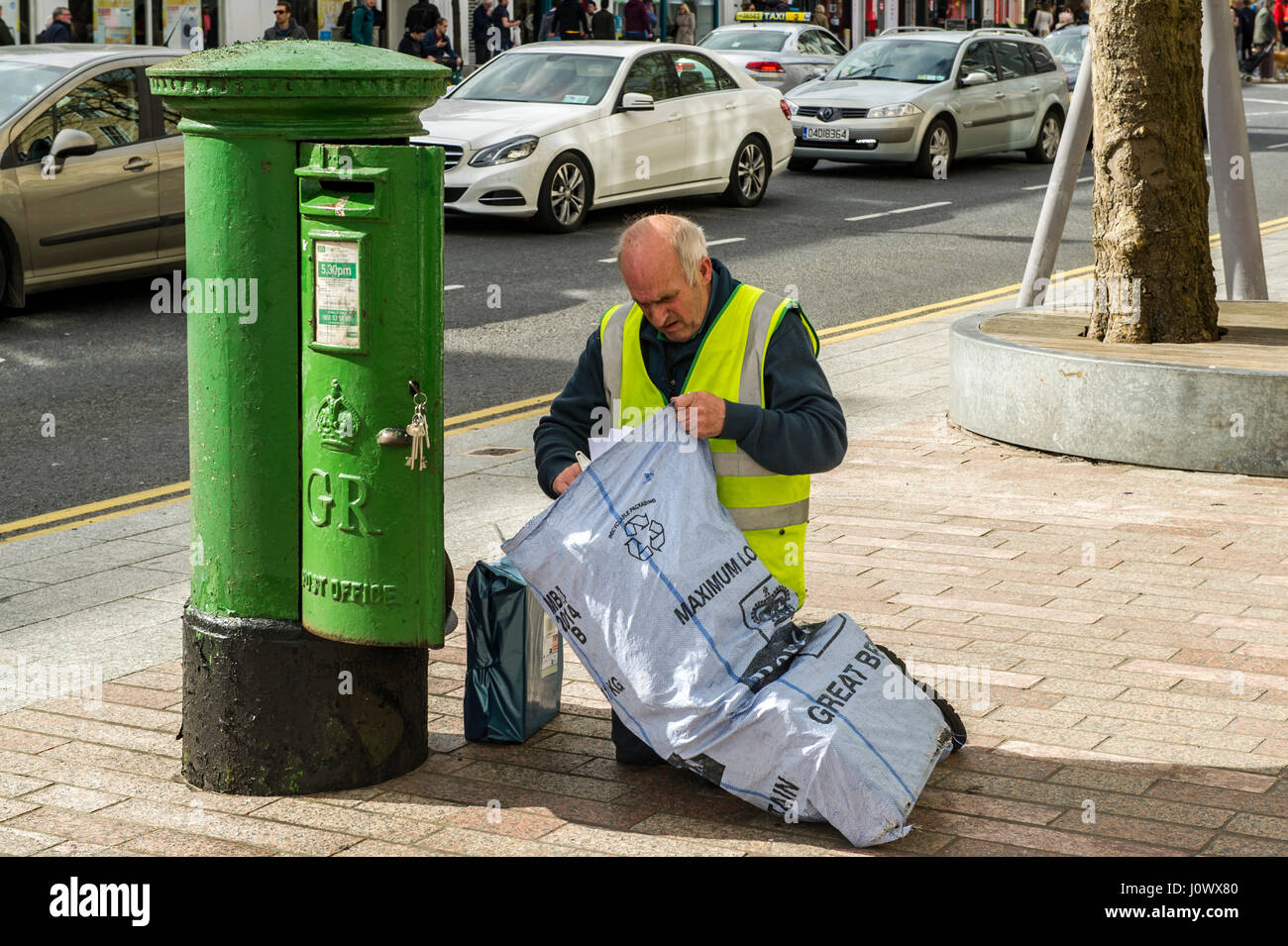 Die irische Post Postbote beim Entleeren eines Post Box und das Setzen der Buchstaben in einen Sack für Lieferung in Cork, Irland. Stockfoto