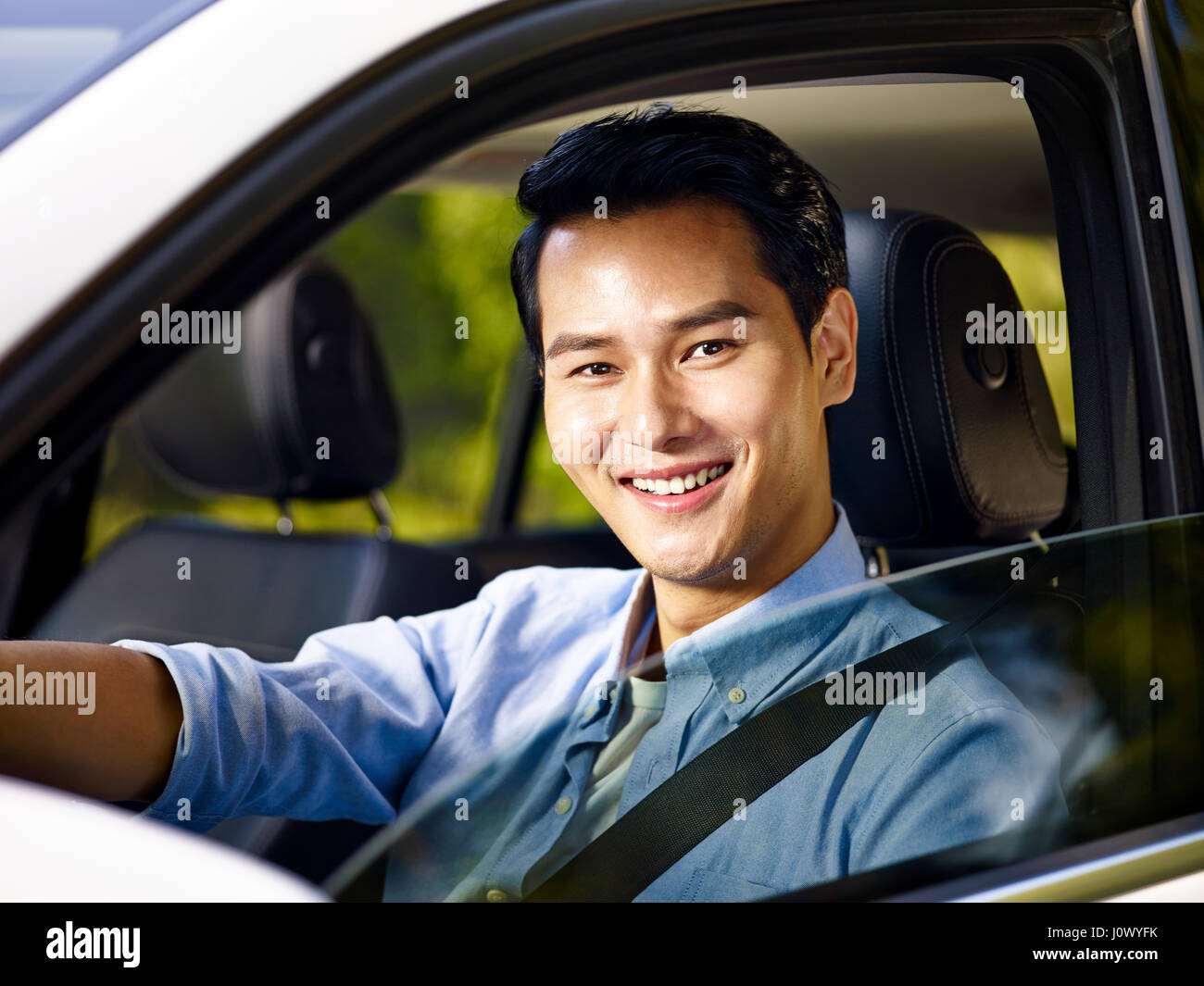 junge asiatische erwachsener Mann sitzen in einem Auto mit Sicherheitsgurt, Blick auf die Kamera zu Lächeln. Stockfoto