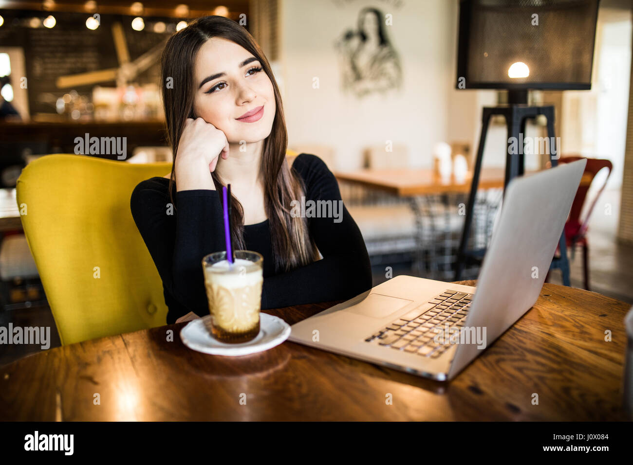 Junge Frau mit süßen Lächeln sitzen mit tragbaren Net-Buch im modernen Café Innenraum während der Freizeit. Stockfoto