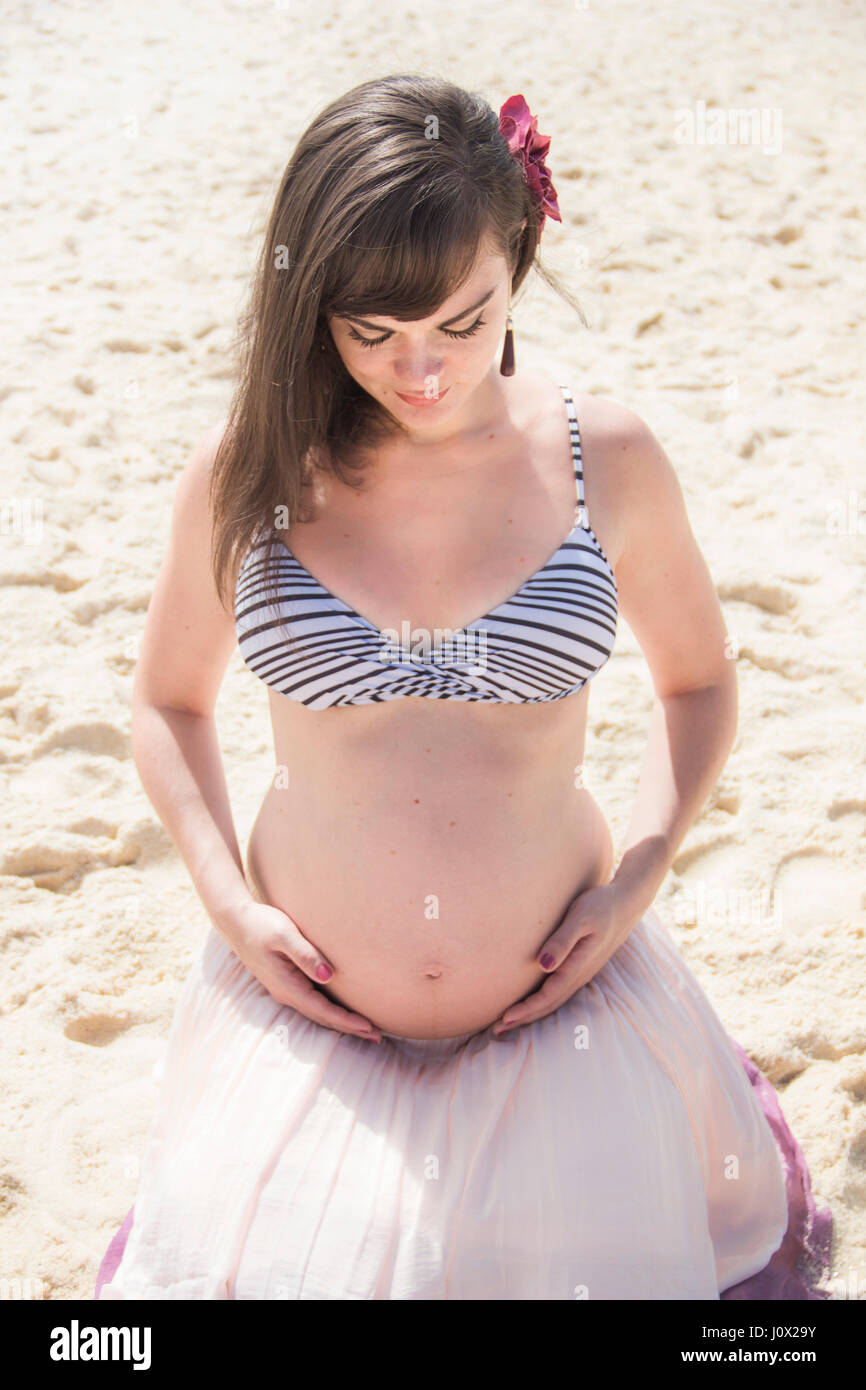 Schwangere Frau sitzen am Strand den Bauch wiegt Stockfoto