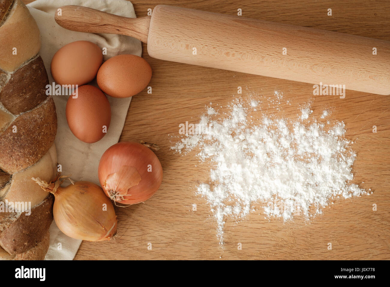Brot mit Zwiebeln, Eiern, Mehl und einem Nudelholz auf einem Holztisch mit textfreiraum geflochten.  Food-Konzept Stockfoto