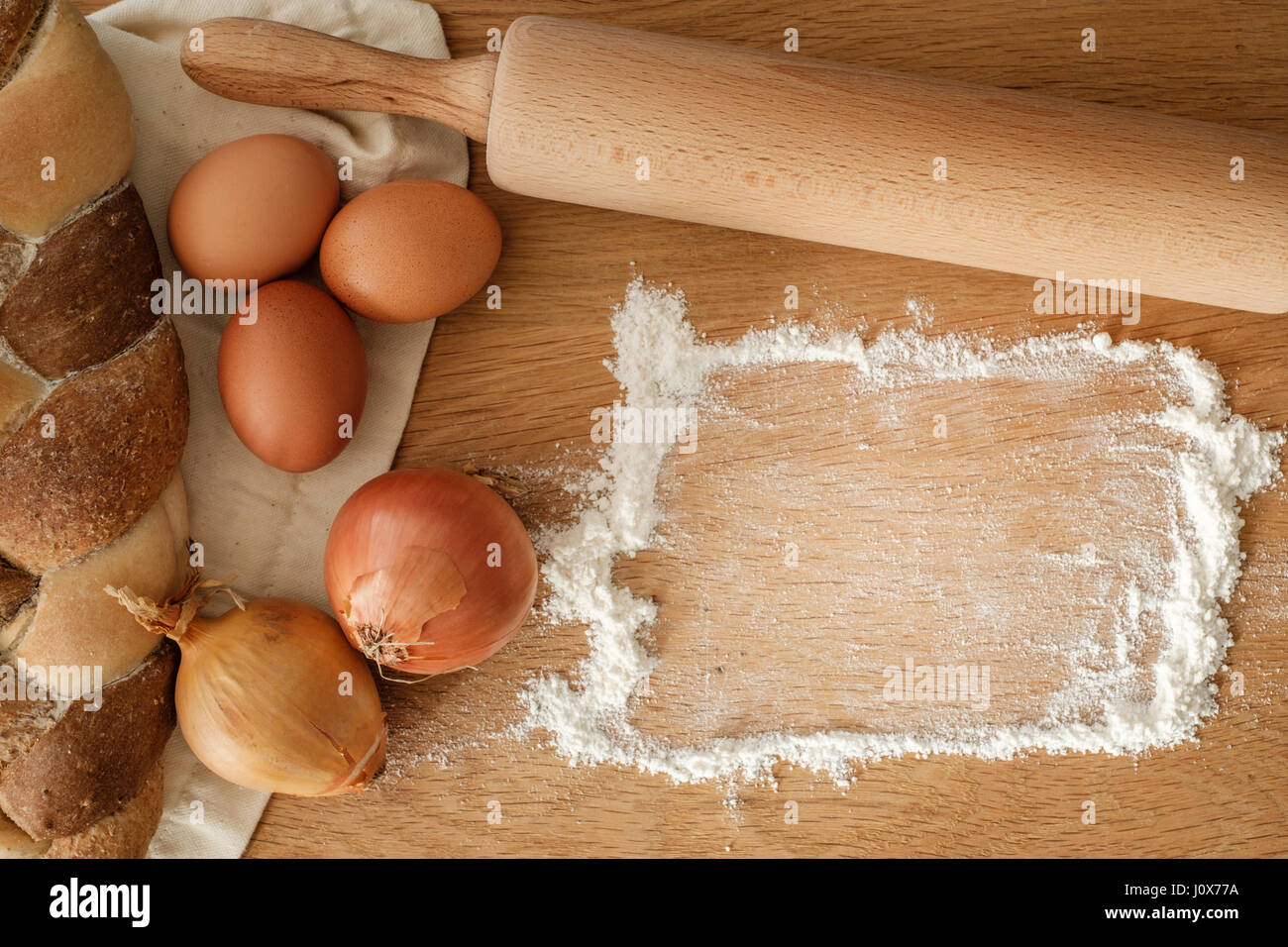 Brot mit Zwiebeln, Eiern, Mehl und einem Nudelholz auf einem Holztisch mit textfreiraum geflochten.  Food-Konzept Stockfoto