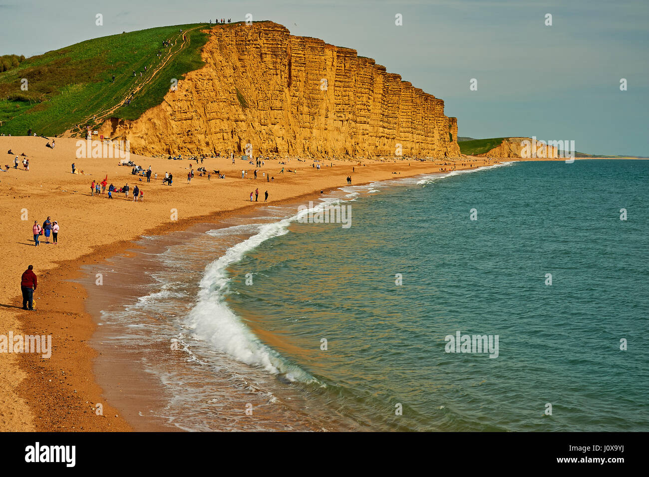 Menschen am Strand von West Bay an der Jurassic Coast in Dorset unter dem hoch aufragenden Felsen von Osten. Stockfoto