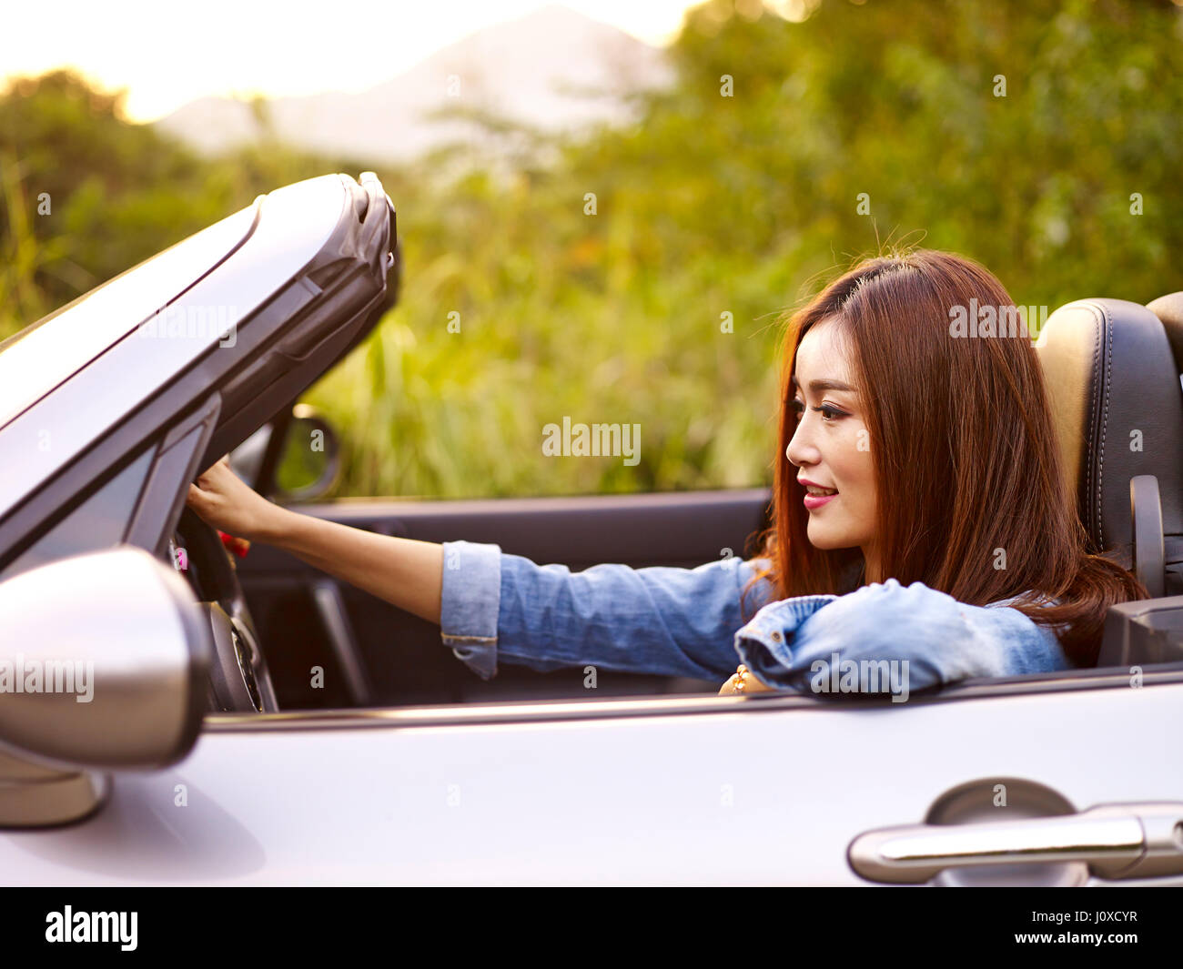 junge asiatische Frau, die Fahrt in einem Cabrio Sport Auto bei Sonnenuntergang. Stockfoto