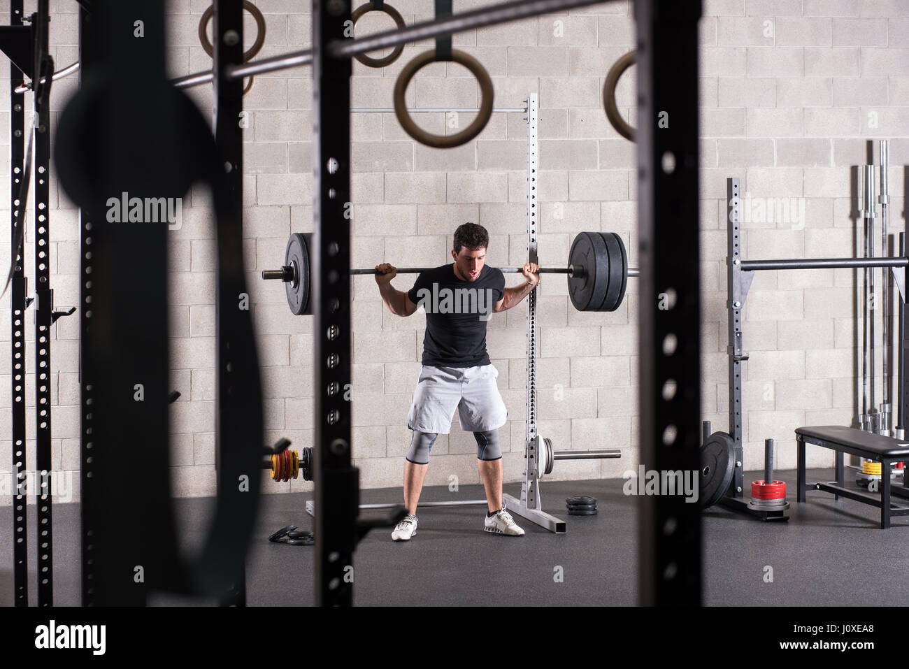 Mann heben schwere Langhantel auf squat Rack, Fitnessgeräte im Vordergrund Stockfoto