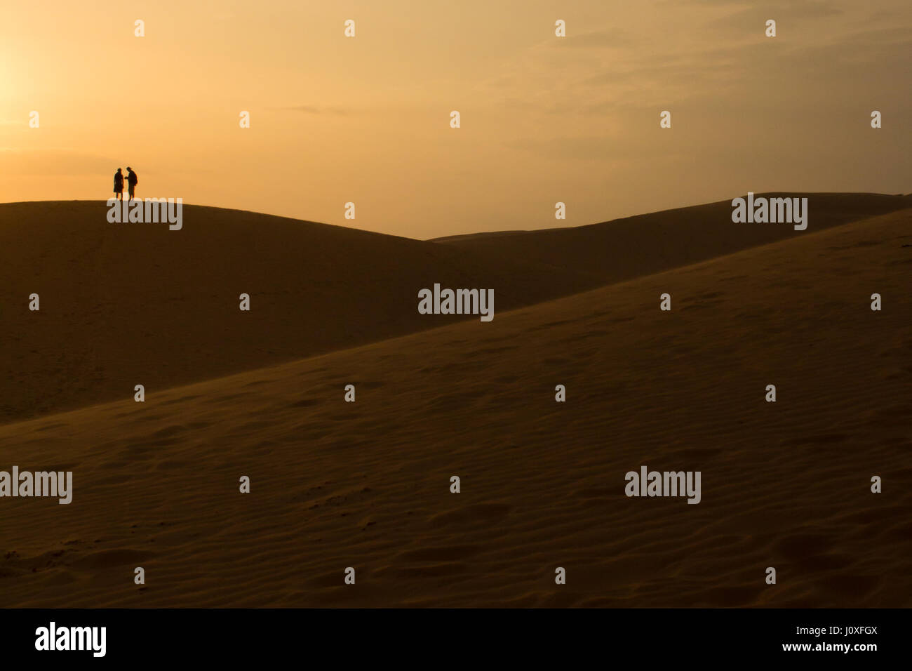 paar auf Sanddüne in der Wüste bei Sonnenuntergang Stockfoto