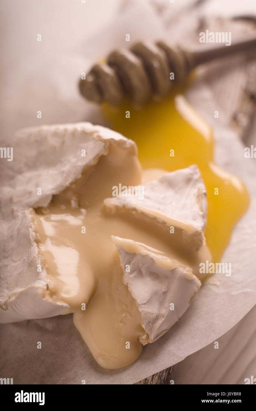 Brie Käse, Scheiben, Honig auf Pergament Unschärfe Stockfoto