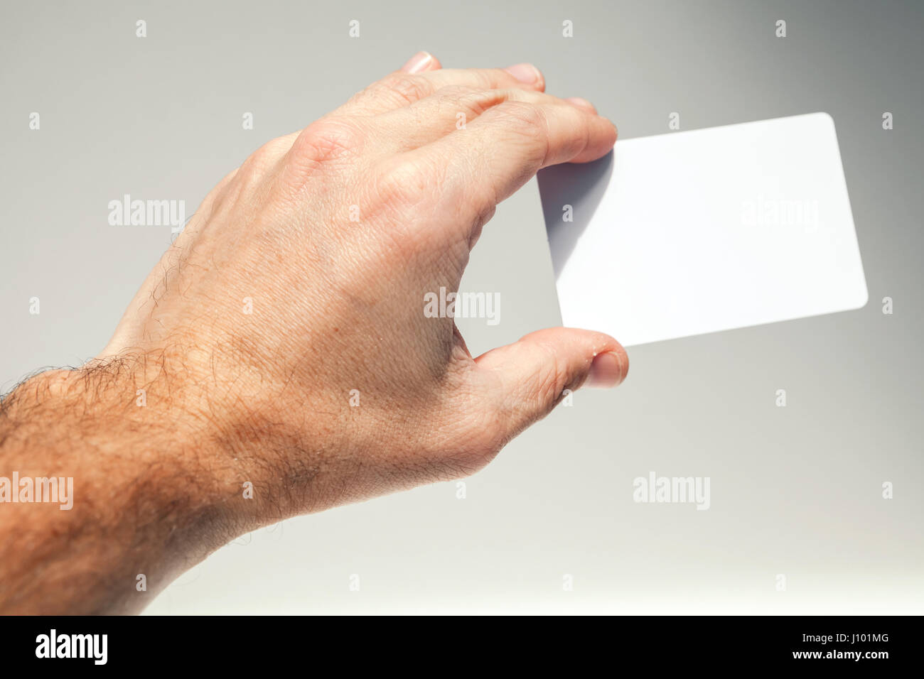 Männliche Hand hält weiße leere Karte über grauen Hintergrund, Nahaufnahme Foto Stockfoto