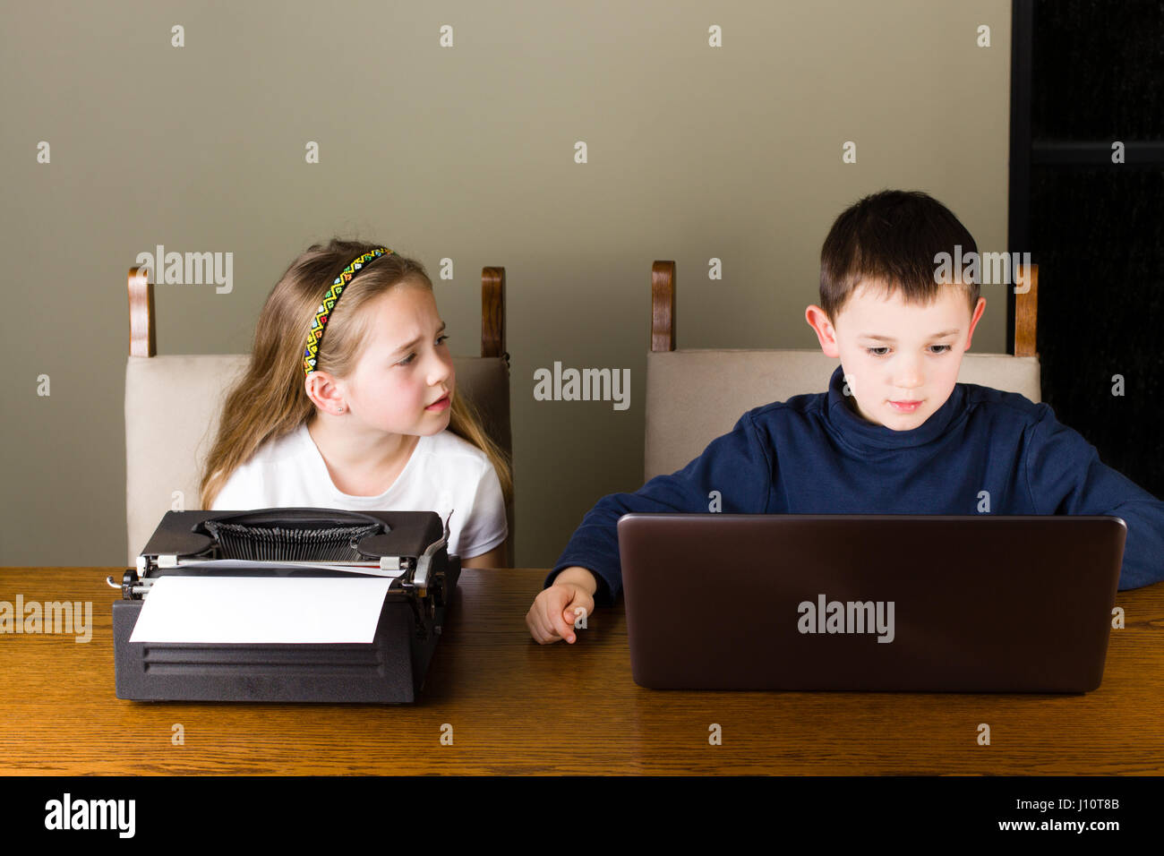 Mädchen eifersüchtig hat sie an einer alten Schreibmaschine zu arbeiten, während ihr Bruder auf einem modernen Laptop arbeitet Stockfoto