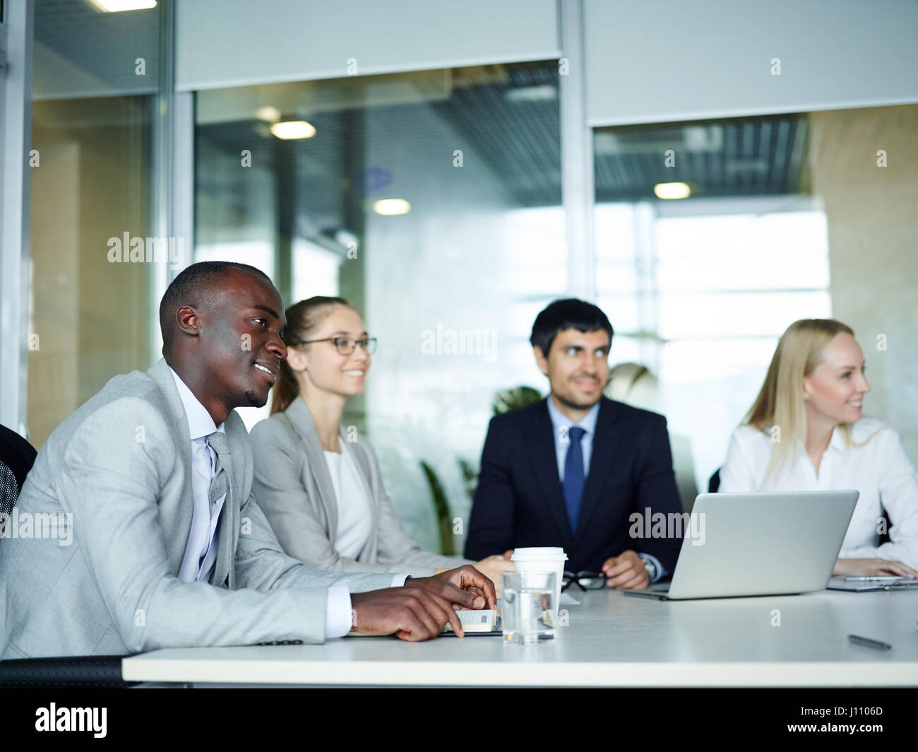 Internationale Gruppe von jungen begeisterten Geschäftsleute lächelnd sitzen Runde Besprechungstisch im Konferenzraum des modernen Büros Stockfoto