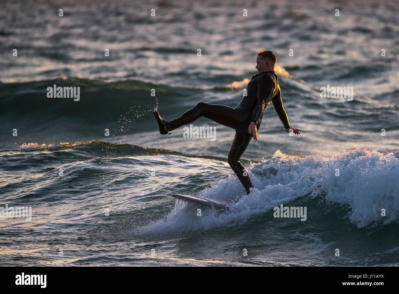 Surfen UK Surfer Fistral Cornwall ungeschickt Balance Balance Welle Surfbrett Sea Spray Abendlicht Wassersport Abend körperliche Aktivität Stockfoto