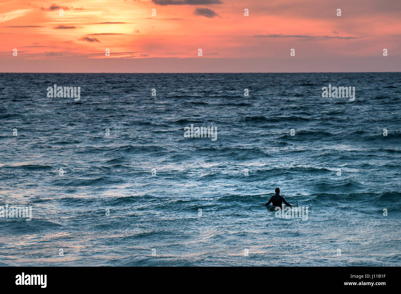 Surfen UK Surfer einsamer Surfer Fistral Cornwall warten für eine Welle Sonnenuntergang intensiver Sonnenuntergang Meer Wassersport Abend Tourismus körperlicher Aktivität Stockfoto